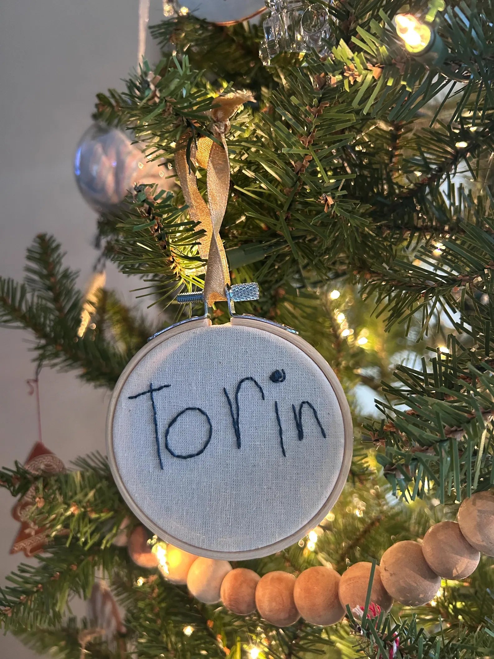 child’s handwritten name custom embroidered ornament on Christmas Tree with light behind